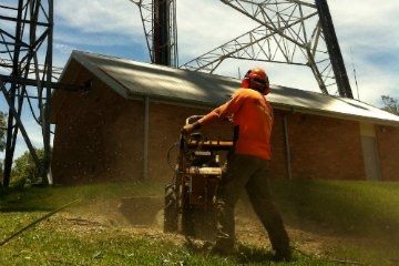 Stump grinder in operation beside a shed