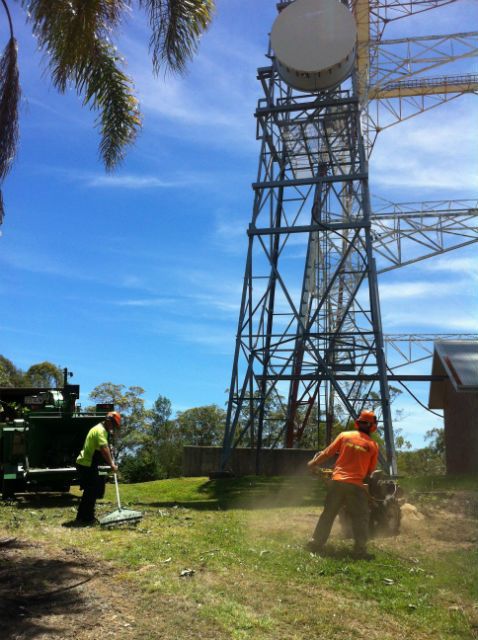 Crew clearing branches below a communications tower, with the wood chipper on site