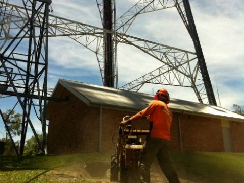Operator running a stump grinder beside a shed